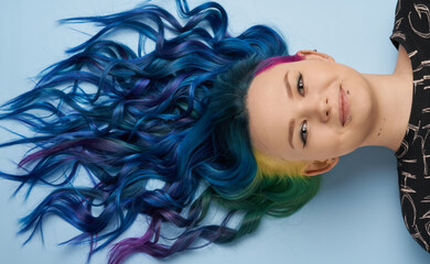 Girl with creative blue coloring and a rainbow in her hair on a blue background. Modern...