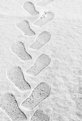 rhythmic boot prints on thin white snow in winter recede into the distance, vertical frame, ribbed protector, winter concept