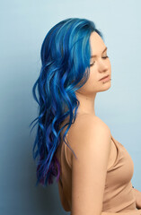 Girl with creative blue coloring and a rainbow in her hair on a blue background. Modern minimalistic bright photography for advertising and social networks