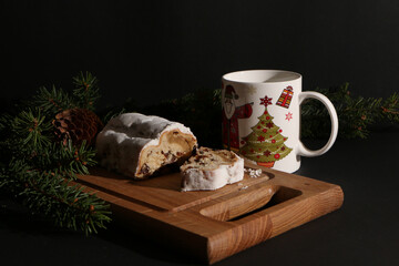 A beautiful Christmas cake, decorated with fir branches with a pine cone and a beautiful cup, on a wooden board. Direct view.