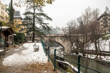 Fototapeta na wymiar Roman bridge (ponte romano - Römerbrücke) on the promenade with snow in winter in Merano South Tyrol Italy