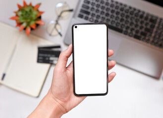 Close - up of a smartphone with a white screen in hand, Notepad in the background, credit cards, selective focus, the concept of online shopping with a phone with copy space, top view.