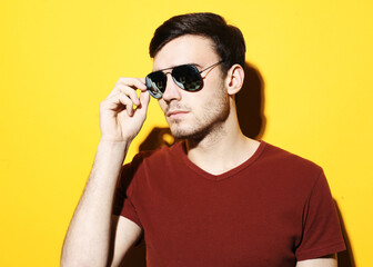 Obraz premium Portrait of a young handsome man wearing sunglasses on yellow background