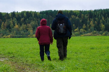 Naklejka na ściany i meble Two travelers are walking along a green field and a dirt road. Family travel