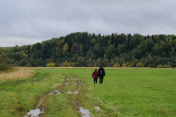 Fototapeta na wymiar Two travelers are walking along a green field and a dirt road. Family travel