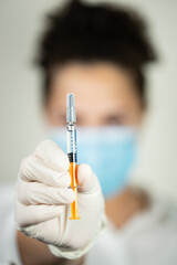 Woman holding a vaccine with gloves and mask.