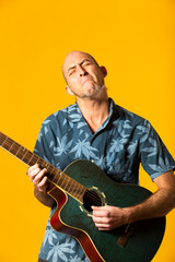 Portrait of a Musician while plying his blue acoustic guitar against a yellow background