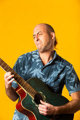 Obraz premium Portrait of a Musician while plying his blue acoustic guitar against a yellow background