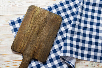 Close up of cutting board with chekered tablecloth on wooden background.