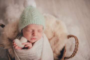 A newborn boy sleeps and holds a white knitted heart in his handles.