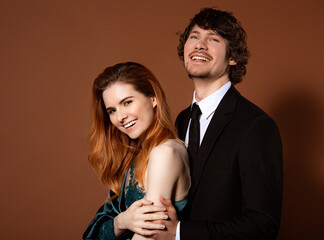 Beautiful red long hair style woman and handsome man with joyful smile celebrating new year holiday on orange bright background. Closeup portrait of laughing