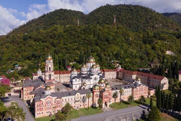 Aerial view of ancient monastery New Athos in sunny summer day, green forest with mountains and church, religious place