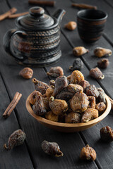 Dried figs in a bowl, on a dark wood surface, teapot on background