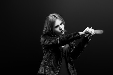 Obraz premium Monochrome studio portrait of young beautiful woman in a leather jacket, red underwear Looks into the camera and beats a wooden baseball bat