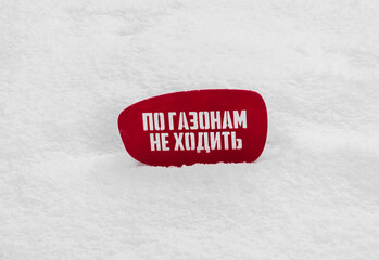 Red notice board on white snow with text in Russian do not walk on the lawns