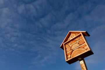 Wooden bee hotel (Insektenasyl) in front of a blue cloudy sky. The facility offers small organisms protection during the winter. Up view. Isolated on blue.