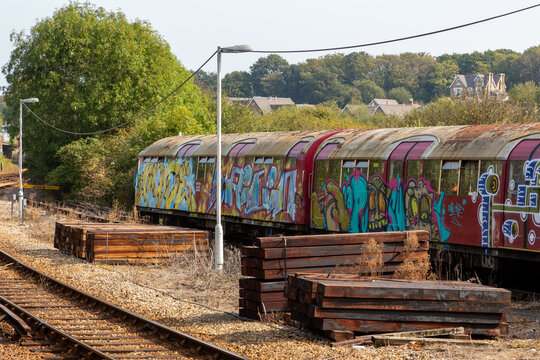 An old underground or tube train covered in graffiti on the side of a train track