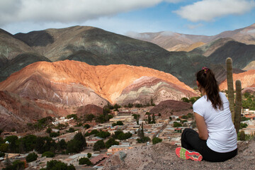 Woman sitting on the mountain, looking at the town of Purmamarca.
