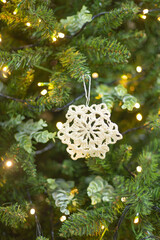 Fototapeta na wymiar snowflake crocheted on the background of a Christmas tree defocused sparkling lights