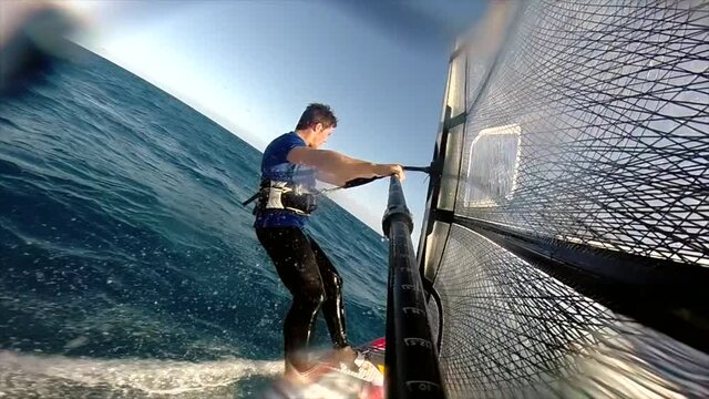 A rear view of an athletic windsurfer sailing very quickly across the bumpy ocean