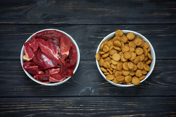  Dog food bowls of raw meat and kibble. Natural raw dog food as opposite of kibble dried food. BARF diet.