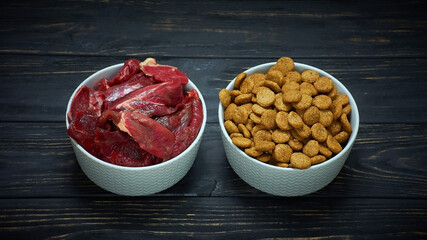 Dog food bowls of raw meat and kibble. Natural raw dog food as opposite of kibble dried food. BARF diet.