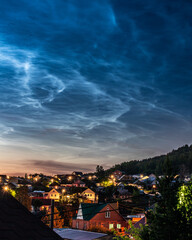 Noctilucent cliuds in the night sky above mountain village in summer
