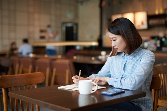 Beautiful young Asian woman writing diary in cafe