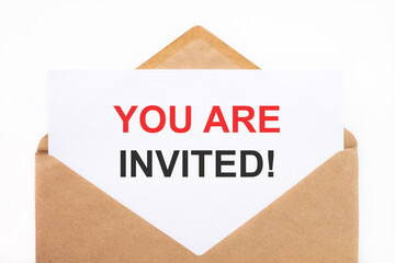 A white sheet with the text you are invited lies in an open craft envelope on a white background with copy space. Business concept image