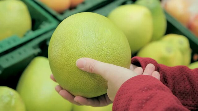Girl in store chooses a large grapefruit from the citrus family. Camera shoots close up. Technical data 4K footage, 25 fps, ProRes 4.2.2, 10 bit color