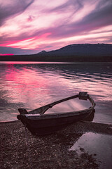 the boat on the shore of the lake after sunset with purple clouds