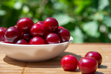 Red cherry berries in a white plate on a bamboo Mat on a blurred background of a green garden. The concept of a healthy vitamin diet