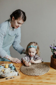 Funny little girl with mother decorating egg with sticker on Easter