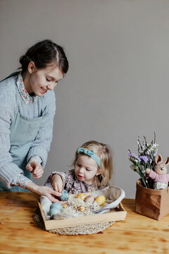 Funny little girl with mother decorating egg with sticker on Easter