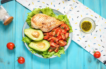 Caprese lunch bowl with grilled chicken and avocado on a blue wooden background. Top view