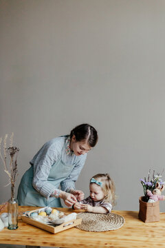 Funny little girl with mother decorating egg with sticker on Easter