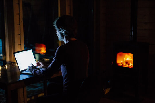 Man working on laptop at night near fireplace