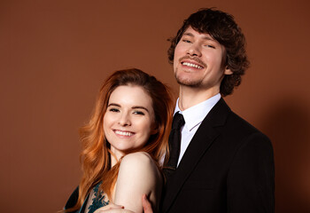 Beautiful red long hair style woman and handsome man with joyful smile celebrating new year holiday on orange bright background. Closeup portrait of laughing