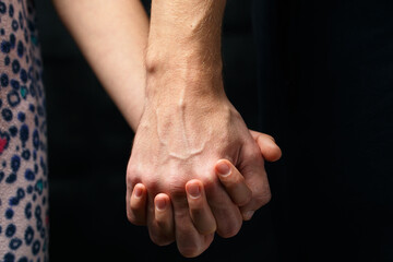 Hand holds childs hand on dark background