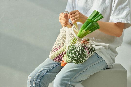 Young woman holding a reusable mesh bag with fresh vegetables.