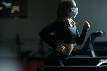 Sportswoman training on treadmill in gym and wearing face mask to protect herself against coronavirus during global pandemic of covid-19 virus