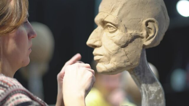Woman sculptor at work on a sculpture of a human head. The process of restoring the shape of the cheek bone. Side view. Close up view.