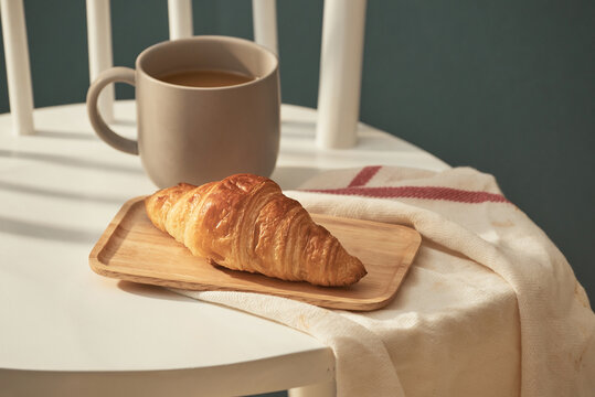 Cup of coffee and croissant on white chair