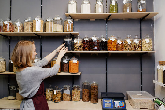 Female seller arranging jars on shelf in organic shop