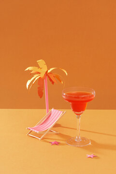 A glass of red wine standing near a summer chair and palm tree on orange.