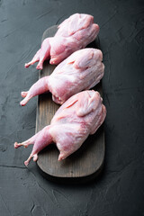 Raw uncooked quails , on black textured background