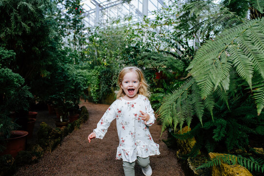 Little Female Kid Running Along Path In Greenhouse