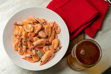 One glass of beer and cooked shrimp on a plate on a yellow background.