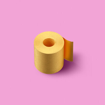Roll of golden color painted toilet paper on a pink background with soft shadows
