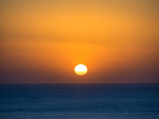 Fototapeta na wymiar Orange sun in the sunset sky over the blue sea